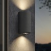 Applique d'extérieur Brixham Wall Twin d'Astro Lighting finition béton charbon allumée sur un mur extérieur de nuit